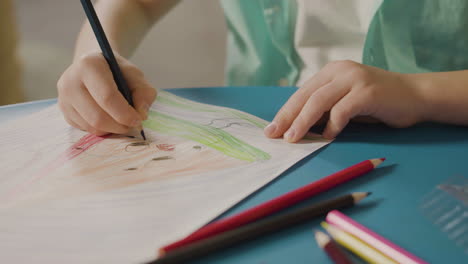 close up of little boy's hands drawing on paper with colored pencil