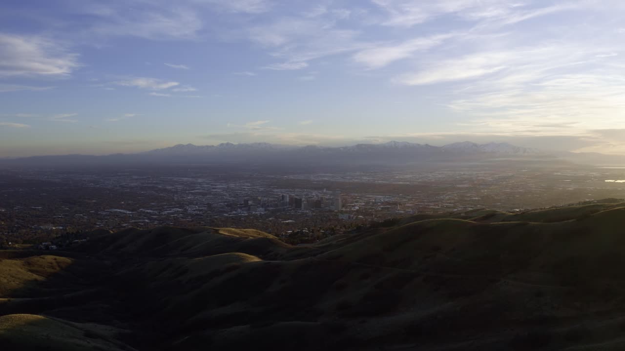 Extreme wide aerial drone shot over the green rolling hills of the bonneville shoreline trail next to Salt Lake City, Utah during a beautiful golden sunset in spring