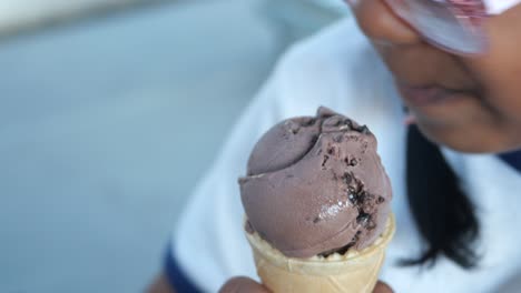 una chica comiendo un cono de helado de chocolate.