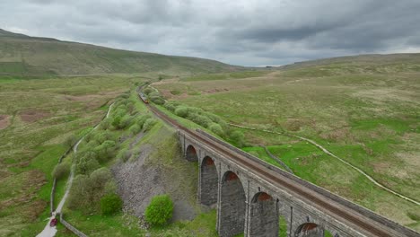 Passenger-train-leaving-viaduct-bridge-and-following-curved-track-into-hilly-moorland