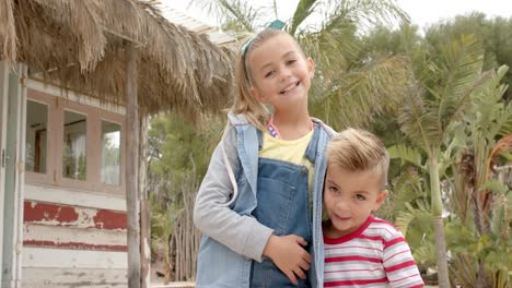 portrait of happy caucasian siblings embracing over palm trees