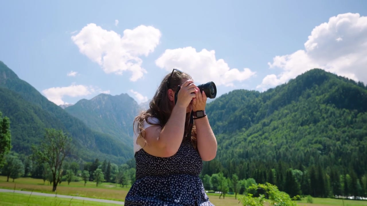 Donna che scatta foto con la sua macchina fotografica mentre è seduta sulla staccionata di legno in Slovenia. - ripresa frontale