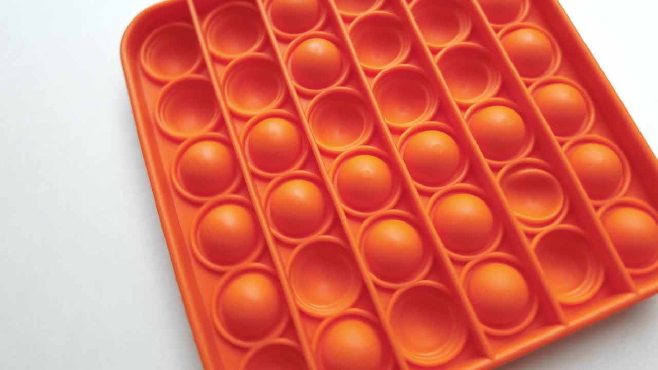nuevo juguete para bebés. pop it juego de dedos. color gracioso. colorido juego girar en la mesa blanca. cuadrado naranja