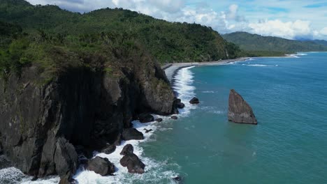 a sweeping drone shot captures a miniature mountain rising beside the ocean, with the waves gently crashing at its base, creating a harmonious blend of rugged and calm coastal beauty.