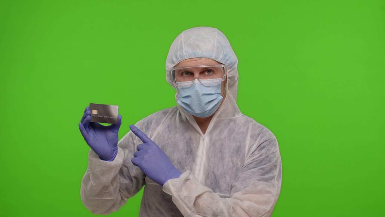 Doctor in PPE suit with coronavirus vaccine ampoule and credit card in hands on green chroma key