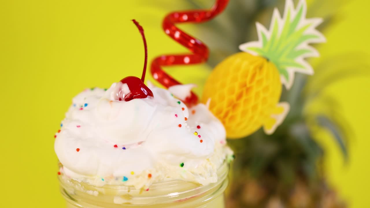 Close-up of hand taking cherry from colorful whipped cream dessert, bright yellow background, static camera