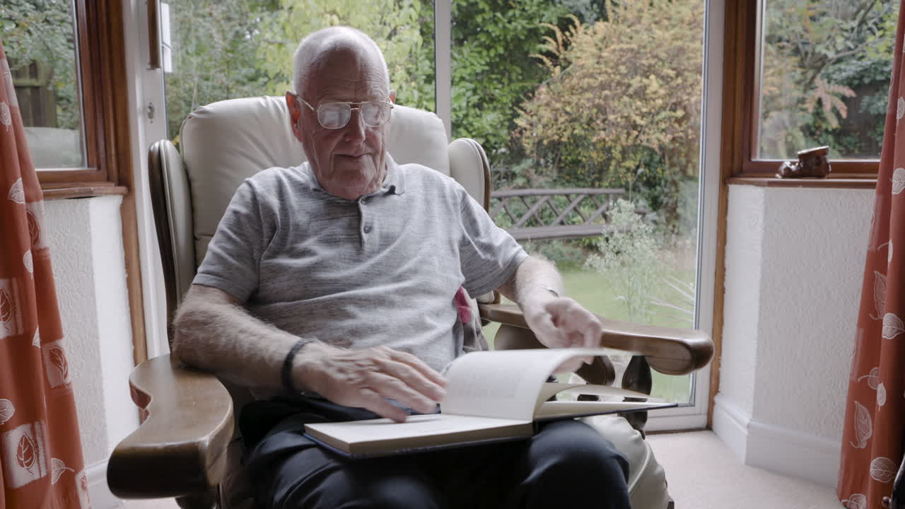 Elderly man sitting in armchair reading a book