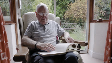 elderly man sitting in armchair reading a book
