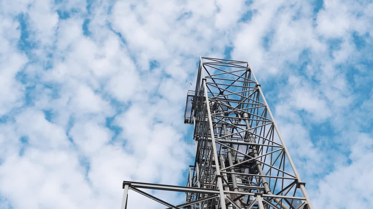 Metal tower against the blue and white sky. Steel construction of a modern factory. Industrial part of a large plant