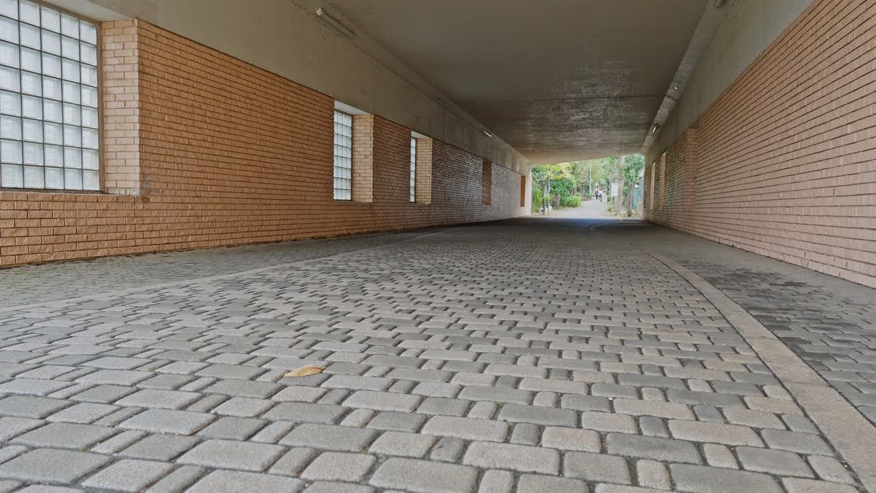 Wide shot of an empty, well-lit pedestrian tunnel with brick walls, glass block windows, and geometric block paver flooring