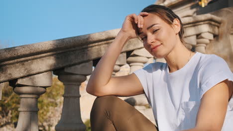 mujer deportiva en camiseta blanca mirando a la cámara descansando en las escaleras en el parque de la ciudad al aire libre.