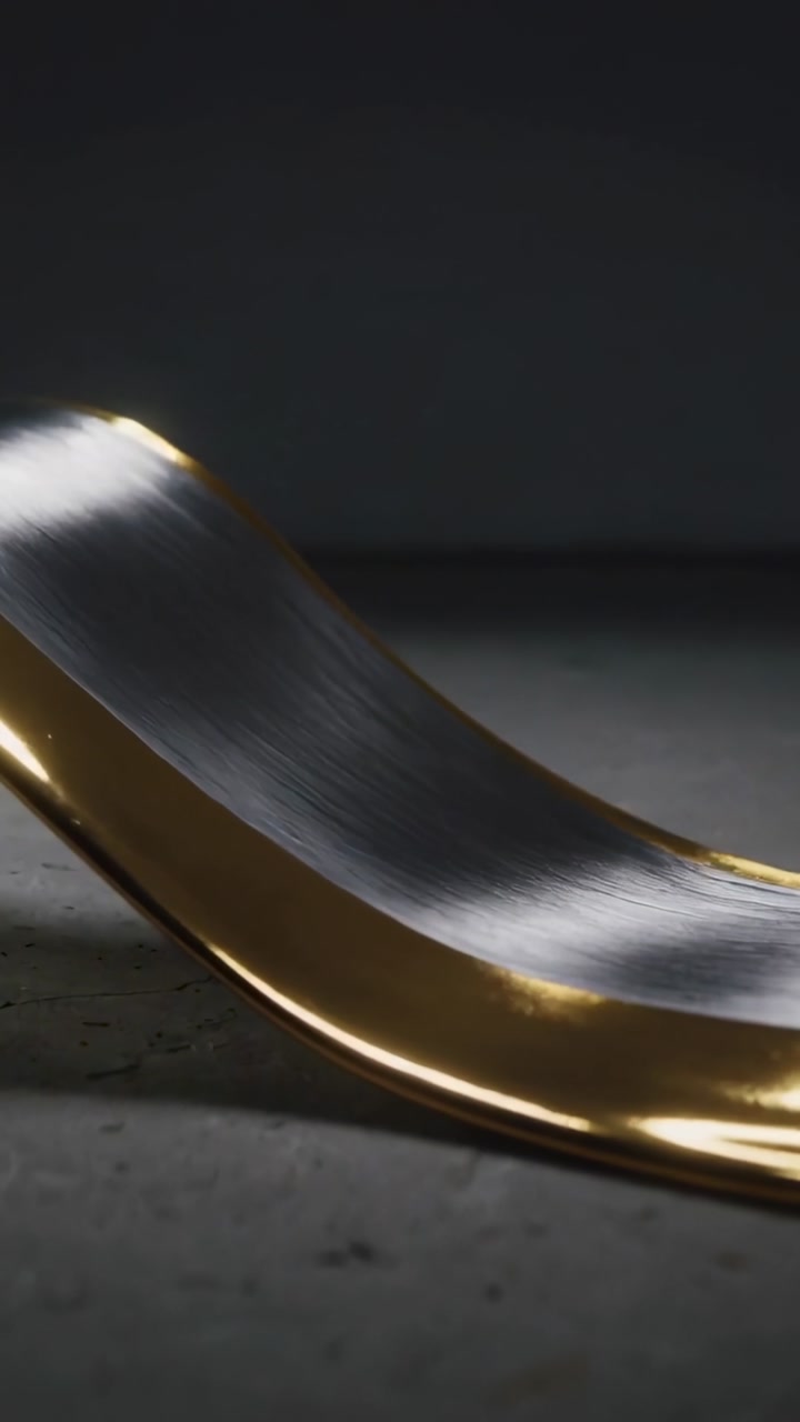 Vertical video: Panning camera revealing curved spoon on gray slab, showing brushed steel gold rim