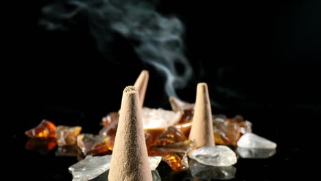 Pushing-past-several-unlit-incense-cones-in-a-decorative-rock-potpourri-garden,-towards-a-lit-cone-with-smoke-billowing