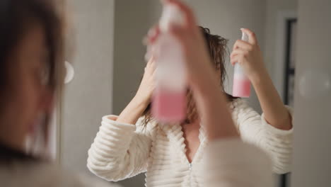 brunette woman splashes spray on hair in domestic bathroom. woman with short hair sprays special product to soften hair after taking shower