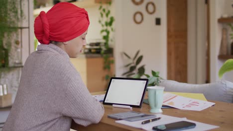 video of biracial woman in hijab sitting at desk at home, working on laptop, copy space on screen
