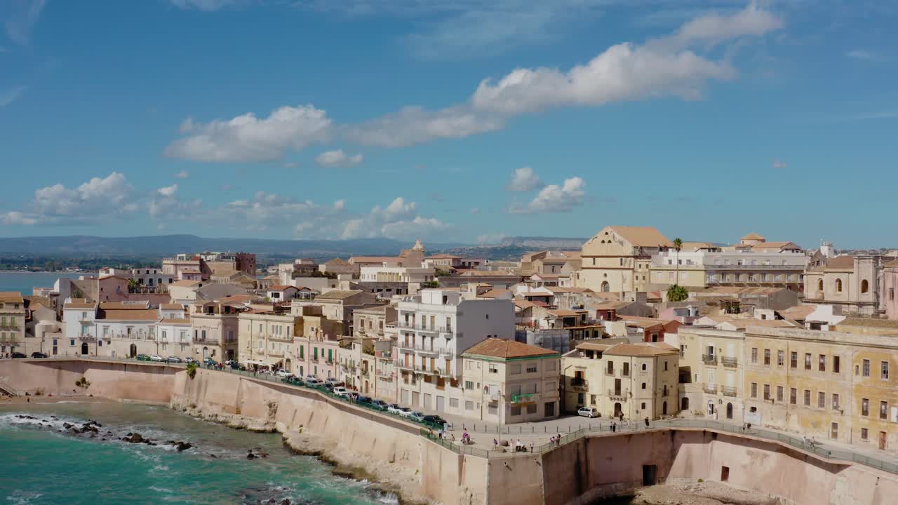 Aerial view of Ortigia island buildings on the coastline. Ascending drone shot above sea with a view to Syracuse. Charming town by the Mediterranean sea in Sicily.
