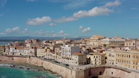 aerial view of ortigia island buildings on the coastline. ascending drone shot above sea with a view to syracuse. charming town by the mediterranean sea in sicily.