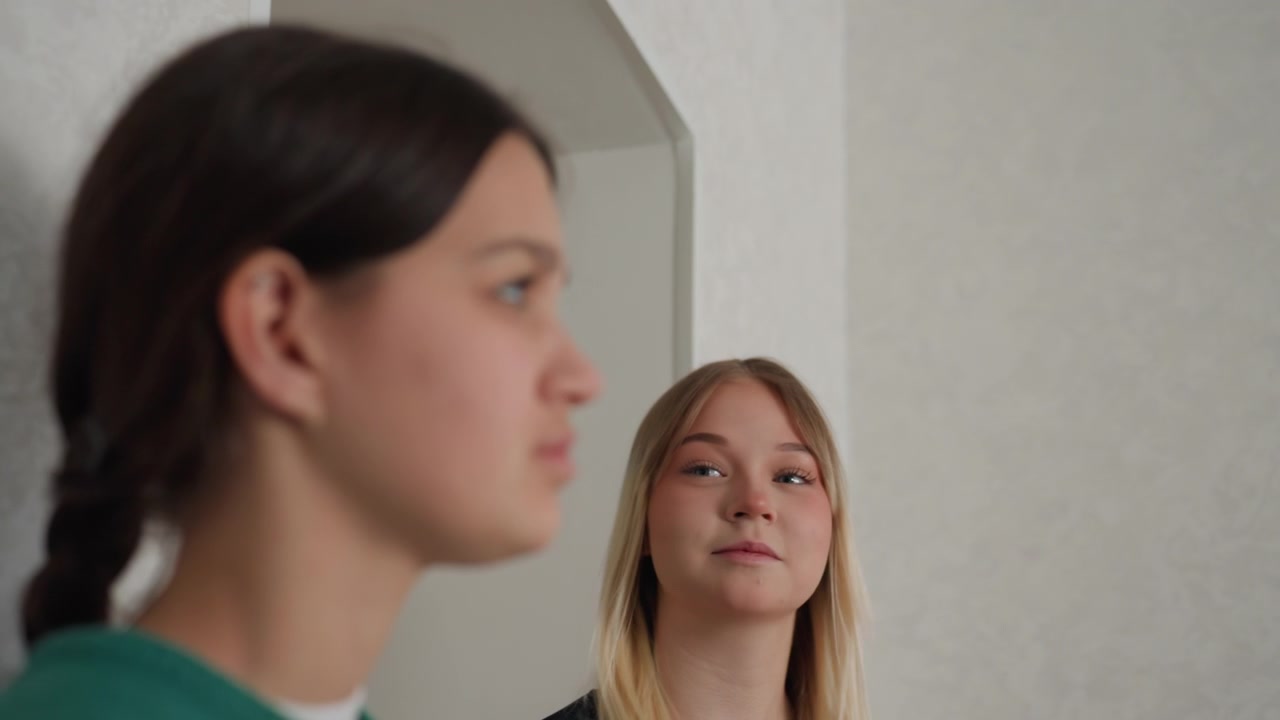 Due donne si fermano sulla soglia dell'appartamento, un momento contemplativo e delicato dopo il trasloco, profili ravvicinati con espressioni calme, un sorriso sottile da una delle coinquiline, pianificazione condivisa e dolce compagnia in un ambiente caldo.