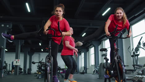 Group-athletic-girls-performing-aerobic-riding-training-exercises-on-cycling-stationary-bike-in-gym