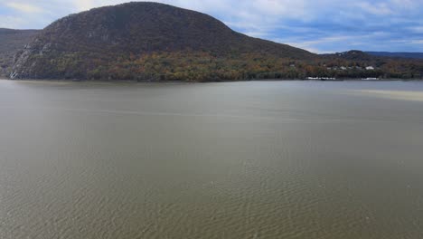 flying sideways down a river valley in autumn with a mountain and village across the water on a windy day