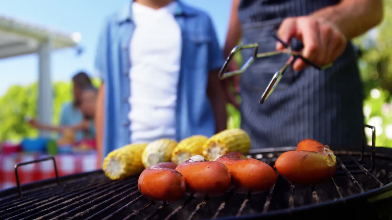 Father and son grilling sausages and corns on barbecue