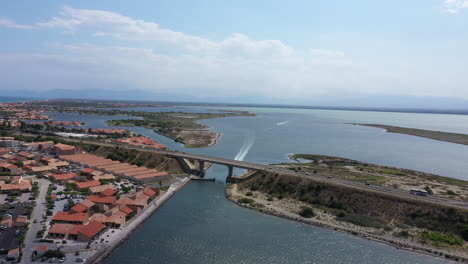 Boot-Fährt-Unter-Einer-Brücke-Hindurch-Leucate-Lakes-Luftaufnahme-Sonniger-Tag