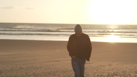 hombre caminando por la playa de arena al atardecer