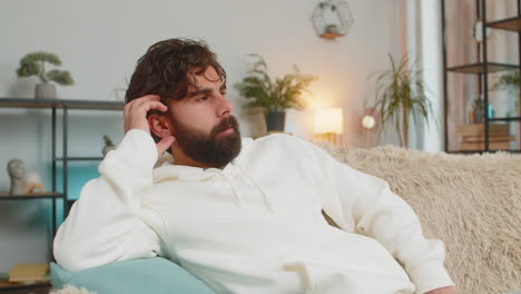 sad lonely indian young man sitting on sofa at home room looks pensive thinks over life concerns