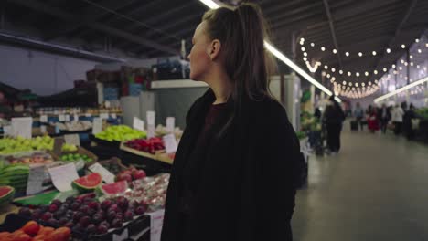 a woman in an indoor market looks at the fruit on offer