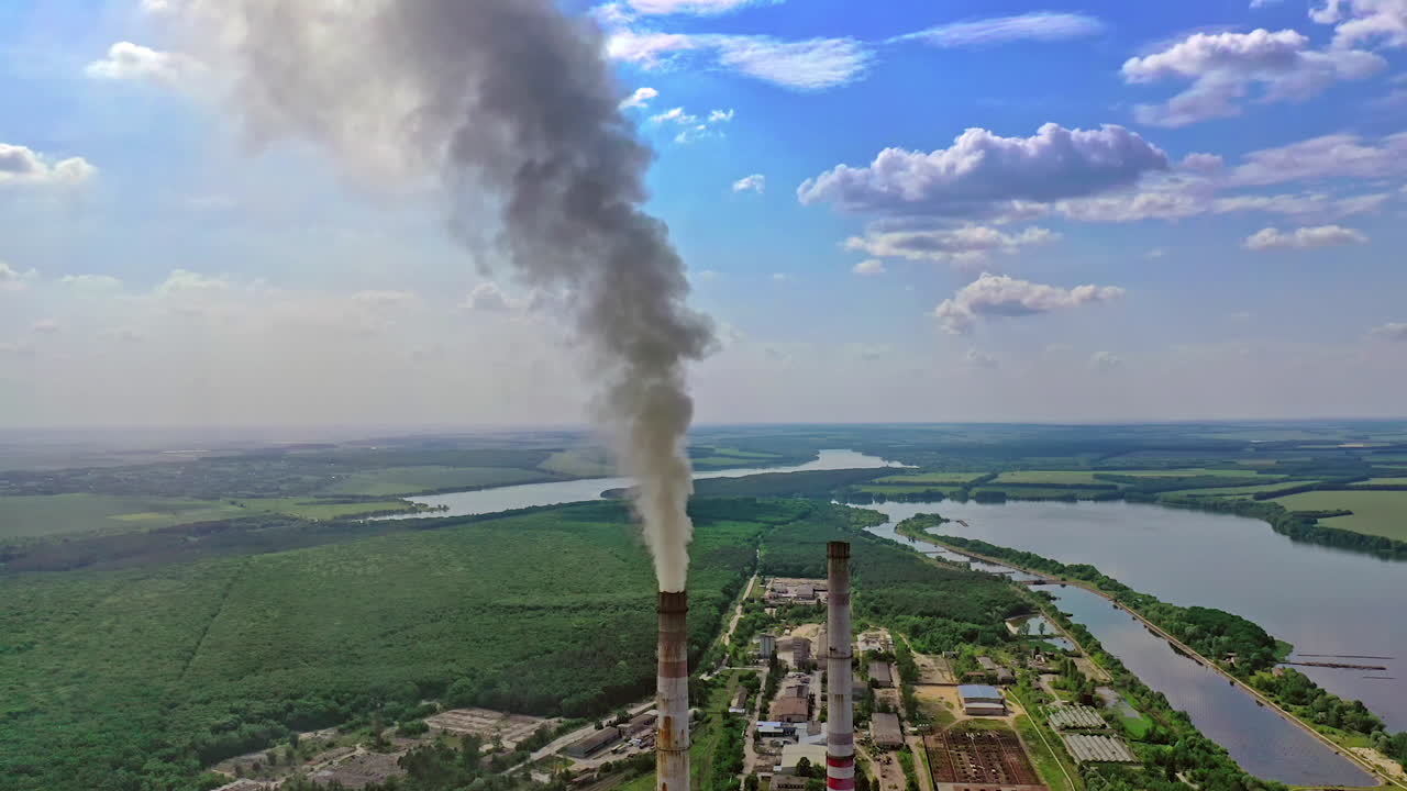 Dirty smoke from industrial pipe. Manufacturing with pipes on nature background with green fields and river. Pollution of environment.