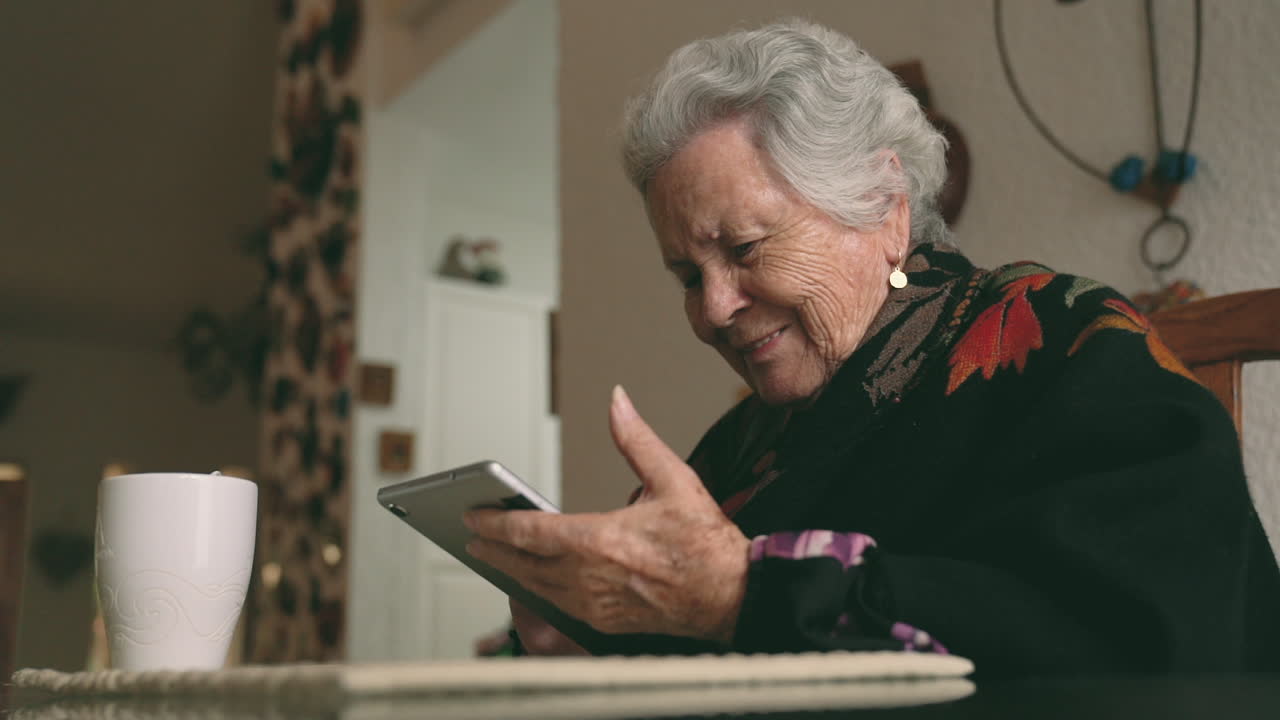 Aged woman with gadget sitting at table