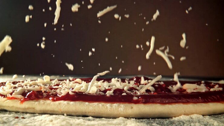 Primo piano al rallentatore di formaggio grattugiato che cade sull'impasto della pizza