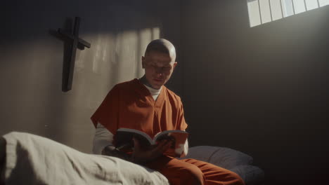 tattooed inmate reading bible on his bed in prison cell