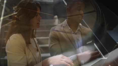 two business people are talking and using a laptop in a corridor of a modern office