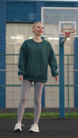 joven practicando voleibol sirve con aro de baloncesto y construcción en el fondo, demostrando la técnica deportiva en la cancha al aire libre