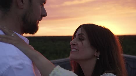 couple kiss each other while the sun is setting behind them and giving an orange look.