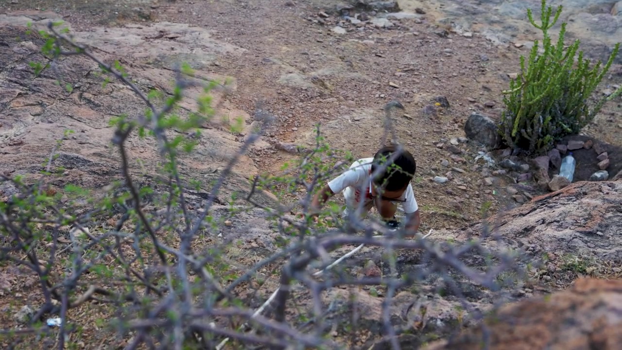 Bambino avventuroso che si arrampica su terreno roccioso con l'aiuto di una corda in un paesaggio selvaggio e arido all'aperto