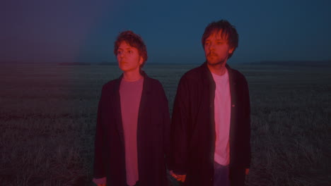 couple holding hands in open field with red illumination at night