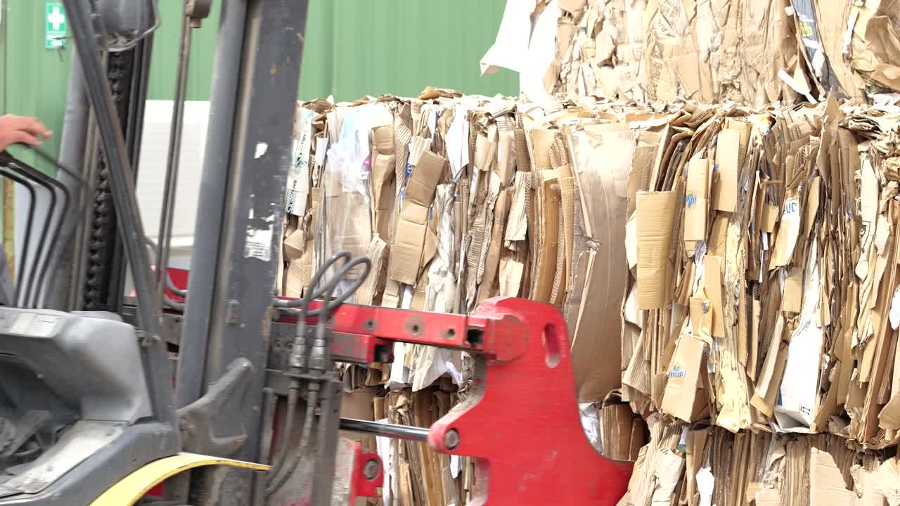 발 클램프를 가진 포크 리프트는 다른 발에 카드보드를 놓고 재활용을 준비합니다.