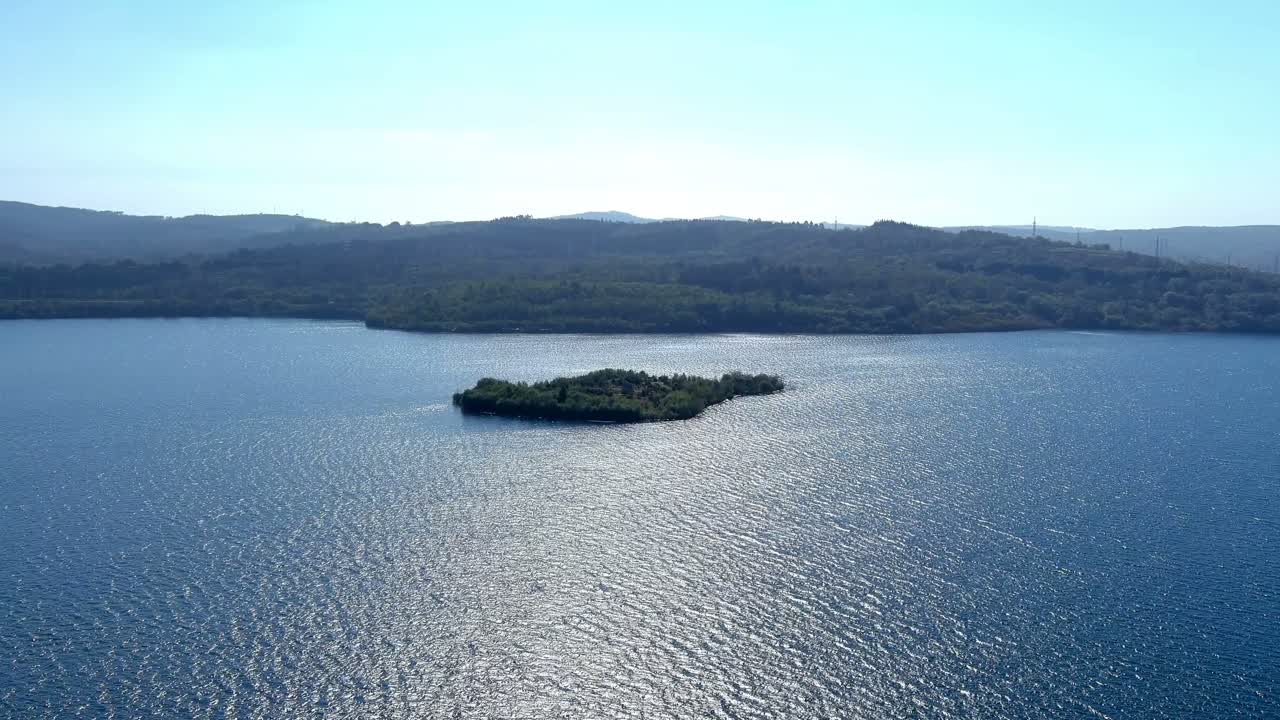 маленький остров с зелеными деревьями посреди озера с сосновым лесом на заднем плане и голубым безоблачным небом в солнечный день