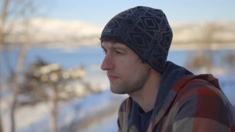 a man in a snow hat calmly sips tea out of a mug with a snowy backdrop