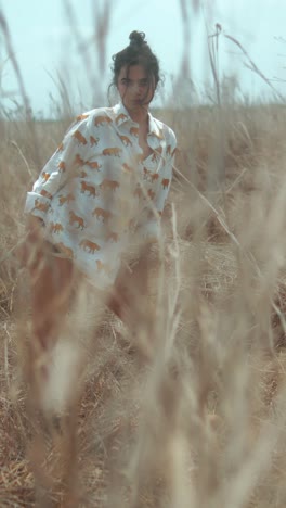 a young woman in a lion-printed shirt poses in a dried grassy field on a sunny day