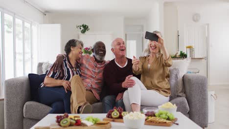 two diverse senior couples sitting on a couch using a smartphone and laughing