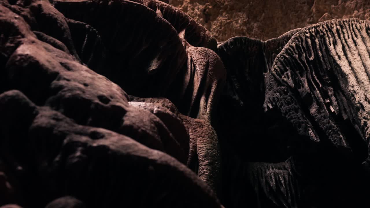 Low angle view inside Ibiza limestone cave showing massive foreground rocks and jellyfish-like flowstone formations illuminated by natural light above