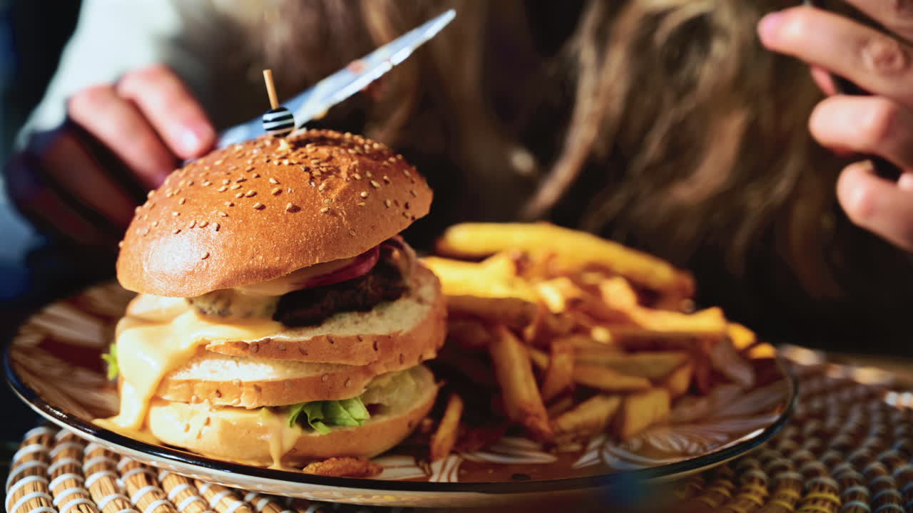 Close up of a freshly prepared cheeseburger with melting cheese as a woman cuts into it with a knife