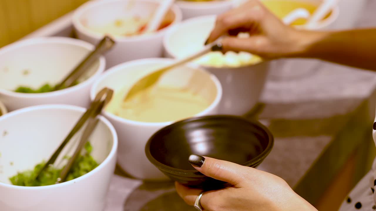 Person scoops creamy sauce into bowl at condiment bar with bright, even lighting, close-up