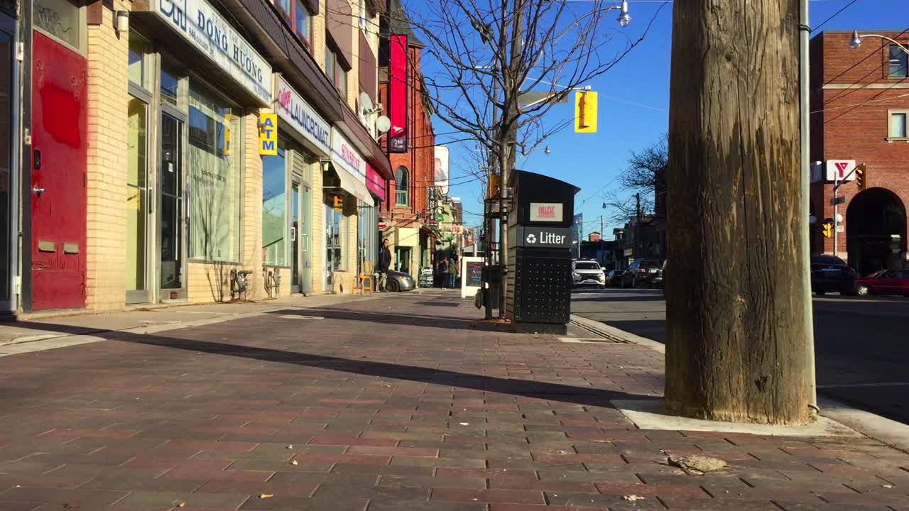 Low angle wide shot on a sunny afternoon, looking east to Dovercourt and College Streets in Toronto, showing vibrancy, traffic and local storefronts