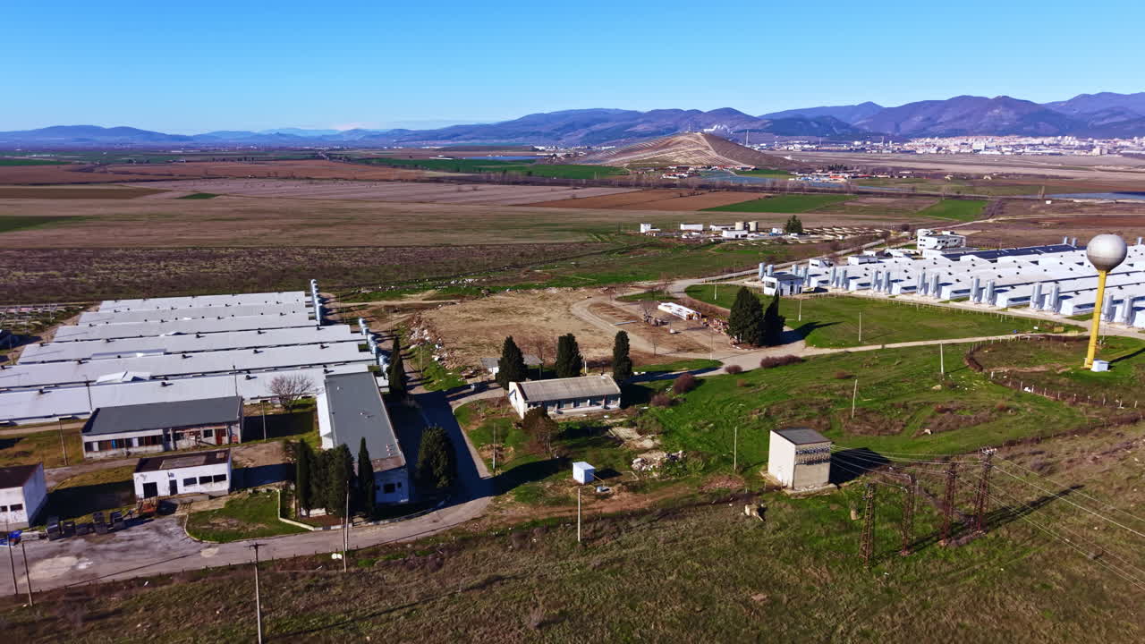Vista aerea di un vasto paesaggio con strutture, campi aperti e montagne sullo sfondo durante una giornata limpida in un contesto agricolo