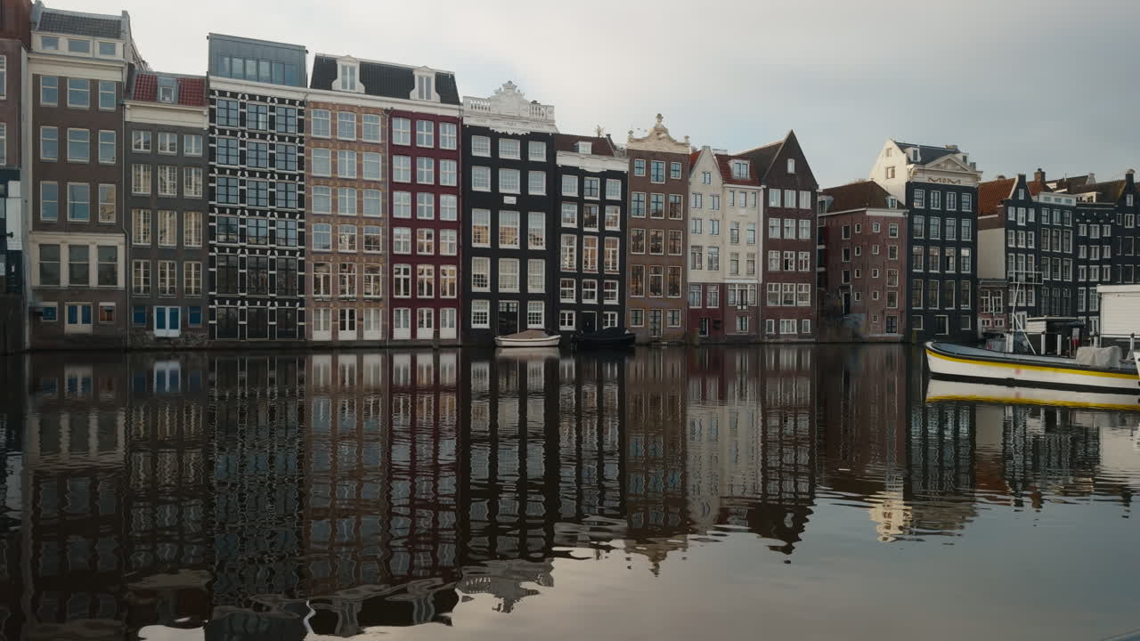 Ikonische Damrak-Grachtenhäuser in Amsterdam, die sich an einem stimmungsvollen, bedeckten Tag perfekt im ruhigen Wasser spiegeln.