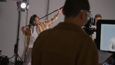 Close-Up-Of-Female-Assistant-Using-Clapperboard-As-Actors-Shoot-Movie-Or-Video-In-Studio-With-Film-Crew-And-Director-Shot-In-Real-Time